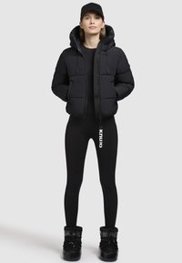 Svart puffjacka med huva och två framfickor, i kombination med svarta leggings och svarta kängor med snören. Enkelt, funktionellt design.