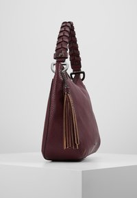 Sac à main en cuir bordeaux avec une finition texturée, une poignée tressée, des garnitures en argent et un détail de pampille décoratif.