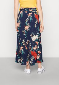 Blommig maxikjol med marinblå bakgrund och röda och vita blommor, tillverkad av lätt tyg och med en svängig design. Kombinerad med vita sneakers.