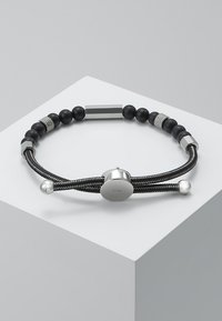 Braccialetto nero e argento con corda intrecciata, perline di metallo lisce e dettagli testurizzati; include una chiusura circolare con logo inciso.
