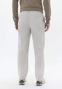 Pantalones de algodón gris claro con cinturilla elástica, que cuentan con dos bolsillos traseros. Llevados con zapatillas blancas y beige.