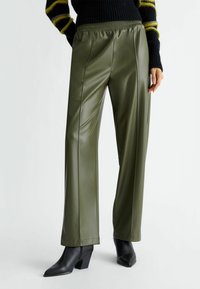 Pantalones de cuero sintético verde oliva con corte holgado, que cuentan con una cintura elástica, costuras frontales y combinados con botines negros.