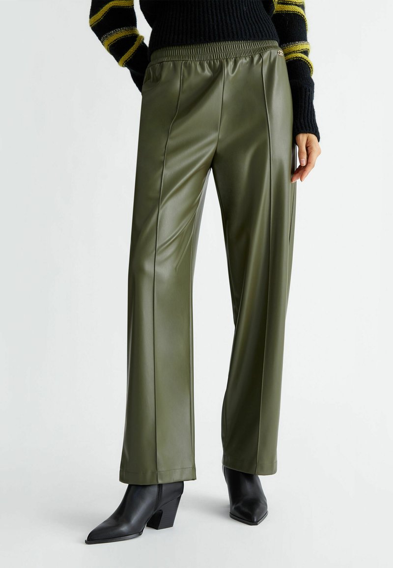Pantalones de cuero sintético verde oliva con corte holgado, que cuentan con una cintura elástica, costuras frontales y combinados con botines negros.