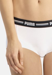 Bikini de algodón blanco con una cinturilla elástica negra que presenta el logo de "PUMA" y dos franjas azules. Tela suave y diseño ajustado.