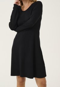 Robe noire à manches longues en tissu doux, avec un col rond et une silhouette trapèze, présentant une texture lisse et des coutures minimalistes.