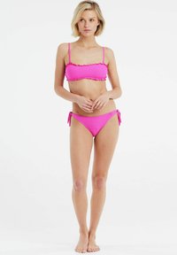 Rožinės bikini komplektas, kuriame yra tekstūruotas bandeau stilius su raukiniais ir derančios užrišamos kelnaitės, parodančios vienalytę spalvą ir minimalistinį dizainą.