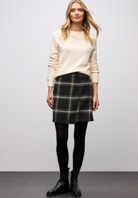 Zwarte geruite rok met een grijs en wit checkpatroon, vergezeld van een crèmekleurige trui en zwarte enkellaarsjes. Zachte stof met een getailleerde pasvorm.
