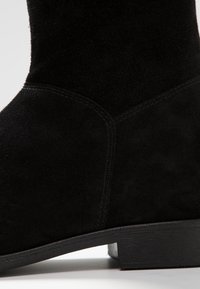 Schwarze Wildlederschuhe mit abgerundeter Zehenpartie, leichtem Absatz und kontrastierenden Nähten an den Seiten, die eine glatte Oberflächenstruktur zeigen.