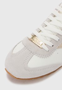 Szürke velúr sneaker fehér bőrbetétekkel, lekerekített orral, fűzős elejével és arany jellemzőkkel, melyeken a "Steve Madden" felirat található.