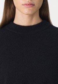 Dunkelblauer Pullover mit einem hohen, abgerundeten Ausschnitt und einem weichen, strukturierten Strick. Eine Nahaufnahme hebt die feine Qualität des Stoffes hervor.