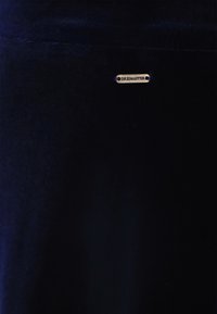 Marine fluwelen stof met een gladde textuur, voorzien van een klein gouden label met de tekst "DREIMASTER" voor branding.