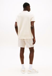 Camiseta de color beige claro con mangas cortas y un escote redondo, combinada con pantalones cortos de rayas claras y zapatillas blancas. Textura suave.