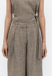 Linnen wikkeltop in een zachte bruine tint, gecombineerd met wijde broekspijpen, met een gestrikte riem, plooien en textuurstof.