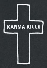 Un tessuto nero presenta un ricamo bianco a forma di croce con il testo "KARMA KILLS" centrato all'interno. Il design ha un aspetto testurizzato e cucito.