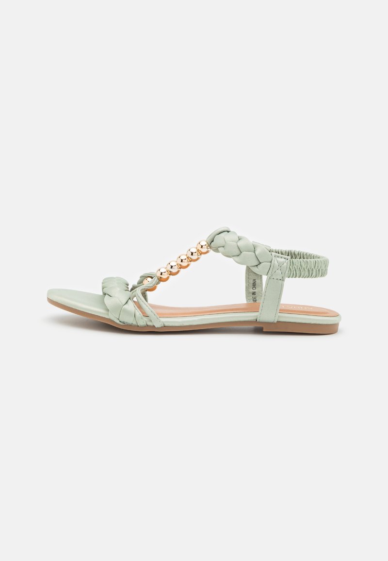 Mintgrønne sandaler med flettede stropper, en guldperleaccent og en flad sål. Designet med en elastisk hæl for fleksibilitet.