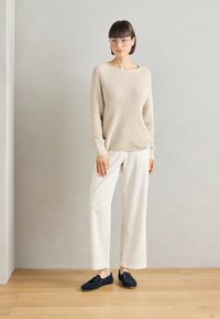 Beige ribbattu knitti t-paita, valkoiset leveälahkeiset housut ja tummansiniset mokkakengät. Mallilla on päällään kirkasraamiset silmälasit. Yksinkertainen, rento asu puulattialla.
