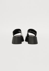 Black block-heeled sandals with an open back, featuring glossy upper material and wide straps for secure fit. Smooth texture and minimalist design.