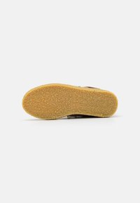 Brown shoe sole with a textured surface, featuring a yellow rubber outsole and a rounded shape. Flat and wide with no visible patterns.