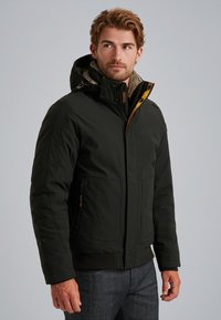 Giacca nera isolata con cappuccio foderato in pelliccia, chiusura frontale con zip e tasche laterali. Presenta un morbido rivestimento interno e polsini regolabili.