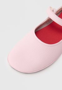 Ροζ δερμάτινο φλατ με στρογγυλή μύτη, που διαθέτει φαρδιά λουρίδα κατά μήκος της πελματιαίας χώρας και αντιθετική κόκ�κινη εσωτερική σόλα. Λείος υφή.