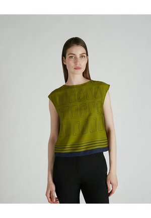 Top verde corto con un motivo geometrico e una striscia orizzontale blu navy all'orlo. Tessuto liscio e maniche a cappuccio. Pantaloni neri indossati sotto.