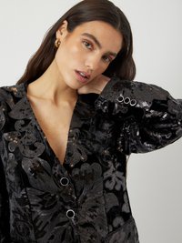 Veste en velours noir ornée de motifs floraux en sequins complexes, dotée d'un col en V profond, de boutons décoratifs et de manches larges.