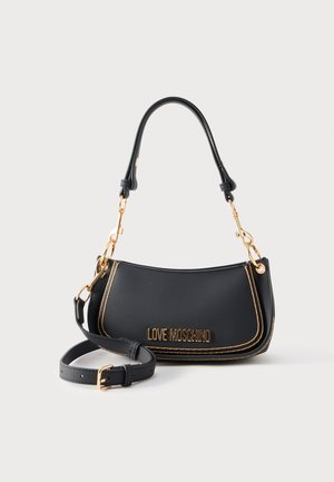 Δερμάτινη τσάντα ώμου Moschino Black Love με χρυσά μεταλλικά στοιχεία, αποσπώμενο μακρύ λουράκι και καμπυλωτή χειρολαβή στην κορυφή, σε γκρι φόντο.