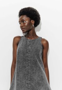 Robe en denim gris au design sans manches. Présente des détails de couture subtils et une coupe décontractée, sur fond blanc.