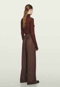 Długi rękaw, dopasowany top w ciemnym burgundzie z wysokim kołnierzem, w połączeniu z szerokimi, wysokimi spodniami wykonanymi z teksturowanej brązowej tkaniny.
