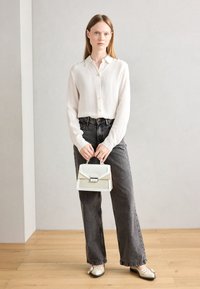 Weißes, knopf-besetztes, geripptes Blusenshirt mit langen Ärmeln; getragen mit dunkelgrauen, hochtaillierten Jeans und einer cremefarbenen Handtasche mit strukturierten Akzenten und silbernen Beschlägen.