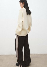 Pull beige en tricot avec ourlet côtelé, associé à un pantalon noir à jambes larges présentant deux bandes verticales beiges. Texture mate sur l'ensemble.