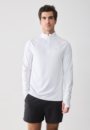 Chemise blanche à manches longues et col zippé quart en tissu léger et extensible, assortie à un short noir. Design simple avec un petit logo sur la poitrine.