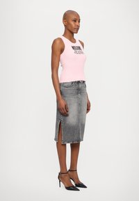 Top de manga ribada numa tonalidade rosa claro com o texto "Moschino Jeans", combinado com uma saia lápis em denim cinza com fendas laterais e sapatos de salto altos pretos.