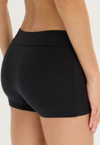Shorts neri elasticizzati con una texture liscia, dotati di una vita ampia e di un taglio aderente intorno alle cosce per comfort e libertà di movimento.