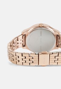 Horloge van rosegoudkleurig metaal met een gestructureerde armband en ronde kast. Witte wijzerplaat heeft minimalistische markeringen en een verhoogde kroon.