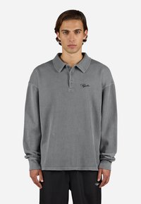 Grå langærmet polo-shirt med ribbet tekstur, knapkrave og broderet logo på brystet, der har afslappede ærmer.