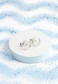 Silvriga vågformade studs visas på en rund vit pedestal med en ljusblå bas, omgivna av blå dekorativa pärlor.