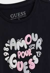 T-shirt nera in cotone biologico con stampa a forma di cuore decorata con testo colorato e strutturato. Include l'etichetta del marchio all'interno del collo.