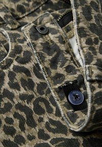 Denimtyg med leopardtryck i nyanser av brunt och svart. Synliga knappar och sömnadsdetaljer med en strukturerad yta.