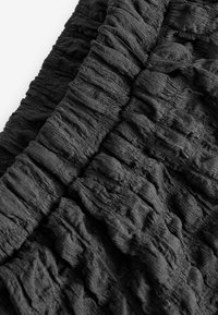 Tela negra texturizada con superficie arrugada, que muestra profundidades y pliegues variados. Material suave y ligero adecuado para prendas de vestir.