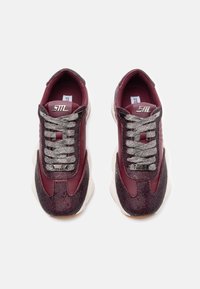 Burgundy sneakers with a textured fabric upper, silver glittery shoelaces, and a thick white outsole. Features logo accents on the tongue.