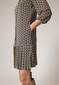 Robe imprimée arborant un motif géométrique en noir, or et crème. Le design comprend un ourlet plissé et des poches latérales.