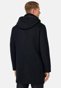 Mornarsko modra kapuca plašč iz mehkega blaga, z dolžino do sredine telesa, čistimi linijami in minimalno opremo. Brez vidnih vzorcev ali dodatkov.