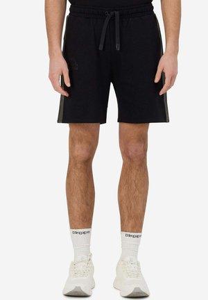 Pantaloni corti neri in cotone con vita elastica, cordino, strisce laterali e dettagli con logo; abbinati a scarpe da ginnastica bianche e calze.