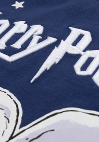 Navystoff mit weiß gesticktem Text "Holy Poly" und Blitzakzenten. Glatte Textur mit leichtem Glanz.