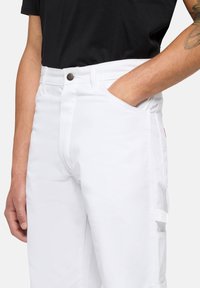 Pantalones cargo blancos con un diseño ajustado, que cuentan con bolsillos laterales, cierre de botón y costuras en contraste. La tela es suave y duradera.