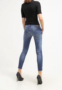 Smala jeans i mediumblå denim med en blektvätt, subtila veck och en läderlapp på baksidan. Matchas med svarta högklackade skor.