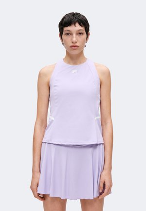 Femme aux cheveux courts et foncés, portant un haut de sport sans manches violet clair et une jupe plissée assortie, face à l'avant sur un fond uni.