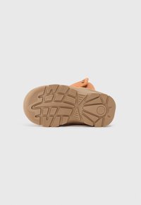 Oransje sandal med en teksturert gummisåle. Bunnen har et sikksakkmønster for bedre grep, med et rundt logo i sentrum.