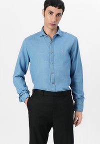 Camicia in denim azzurro chiaro con colletto button-down, maniche lunghe e tasca. Pantaloni neri con chiusura a bottone. Texture liscia e design semplice.